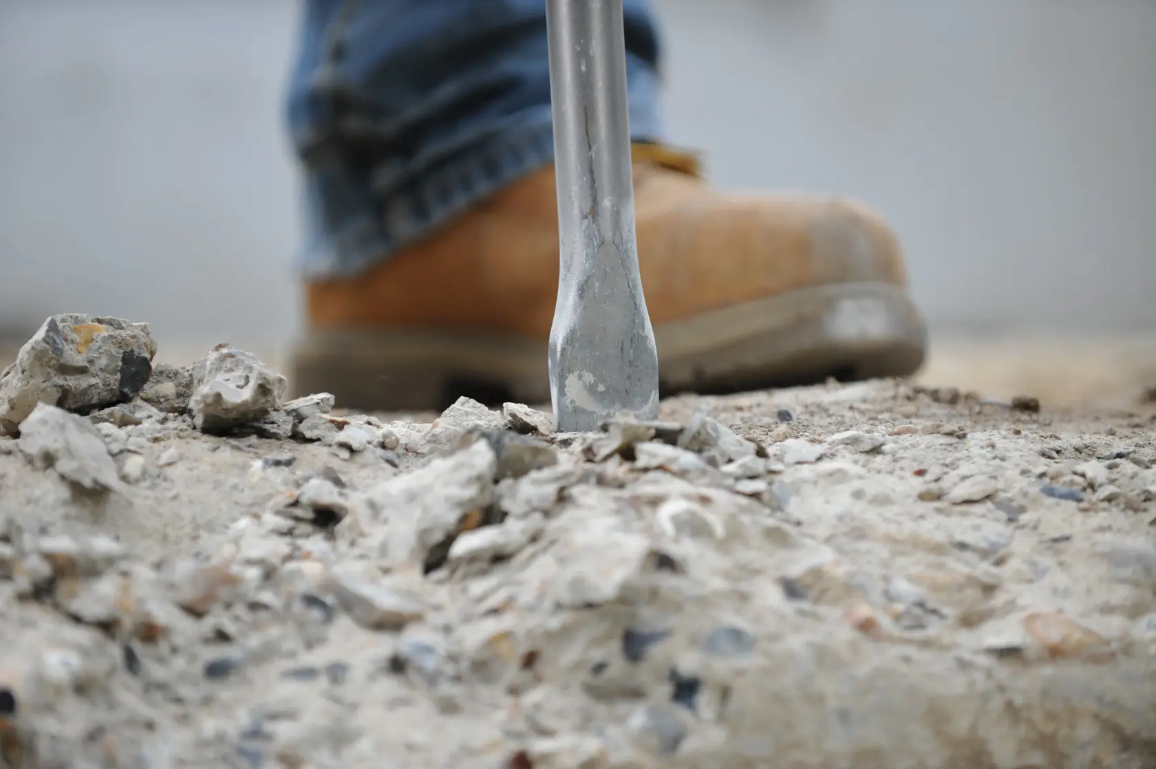Vue rapprochée de la chaussure d'un ouvrier de construction et d'un burin brisant du béton sur un chantier.