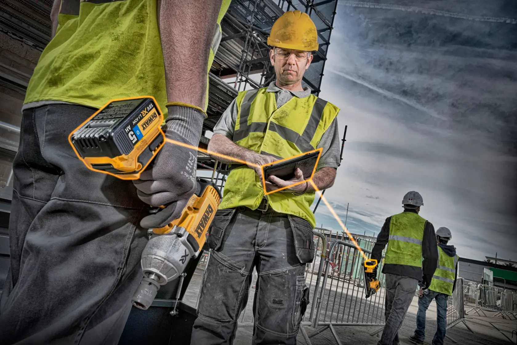 Bauarbeiter mit Sicherheitswesten und Helmen sind auf einer Baustelle zu sehen. Einer hält ein schnurloses DEWALT Elektrowerkzeug, ein anderer benutzt ein Tablet. Im Hintergrund sind Gerüste und Absperrungen sichtbar.