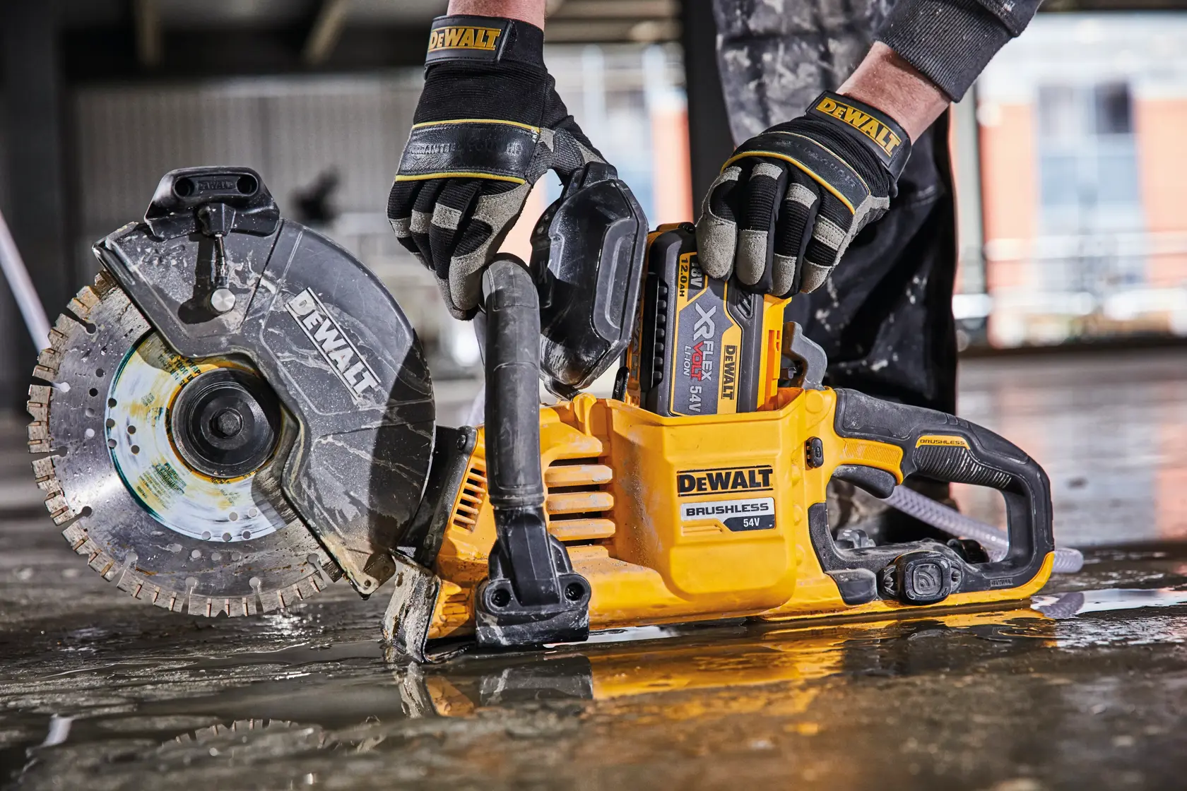 Una persona con guanti protettivi sta utilizzando una sega a disco brushless DEWALT 54V senza fili su un pavimento bagnato da cantiere.