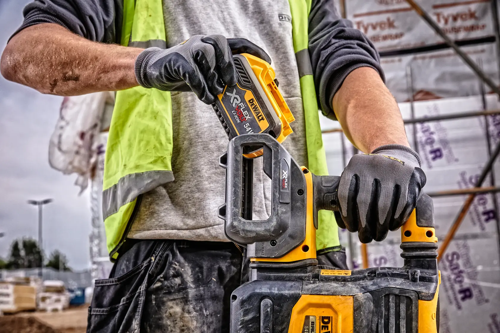 Primo piano di una persona con guanti e gilet ad alta visibilità, che inserisce una batteria DEWALT DCB548 XR FLEXVOLT in un utensile elettrico DEWALT compatibile presso un cantiere.