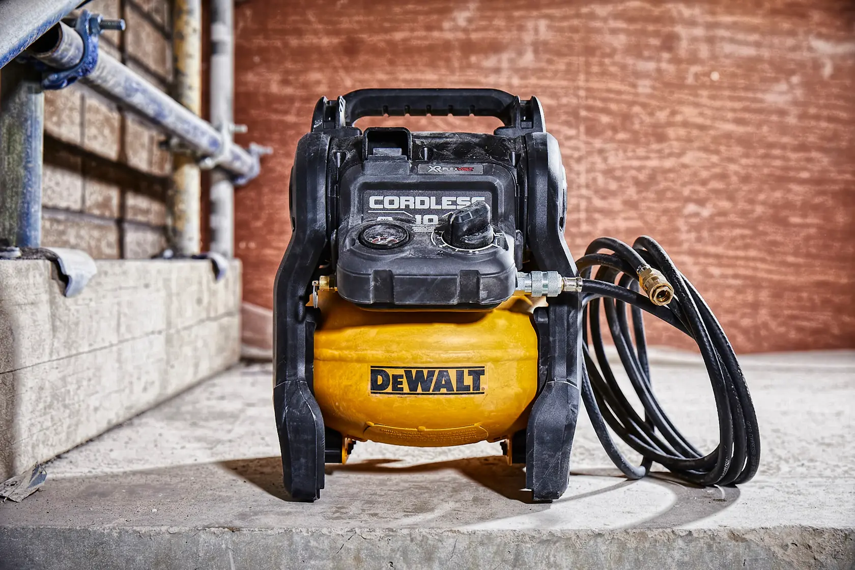 Un compresseur d'air sans fil DEWALT avec une cuve jaune, une poignée noire, un panneau de commande et un tuyau attaché, placé sur une surface en béton dans un environnement industriel.