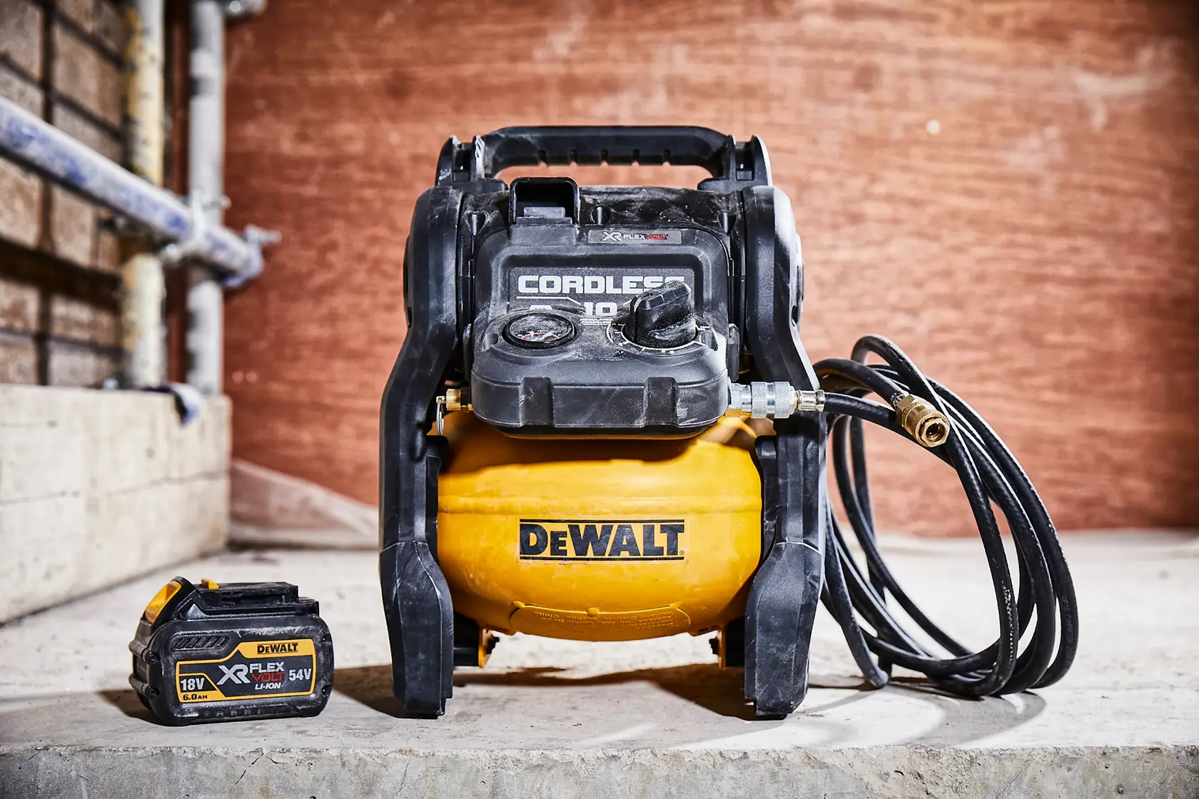 Un compresseur d'air sans fil DEWALT avec un réservoir jaune et un boîtier noir, présenté avec un bloc-batterie amovible. Les deux éléments sont posés sur une surface en béton dans un atelier.