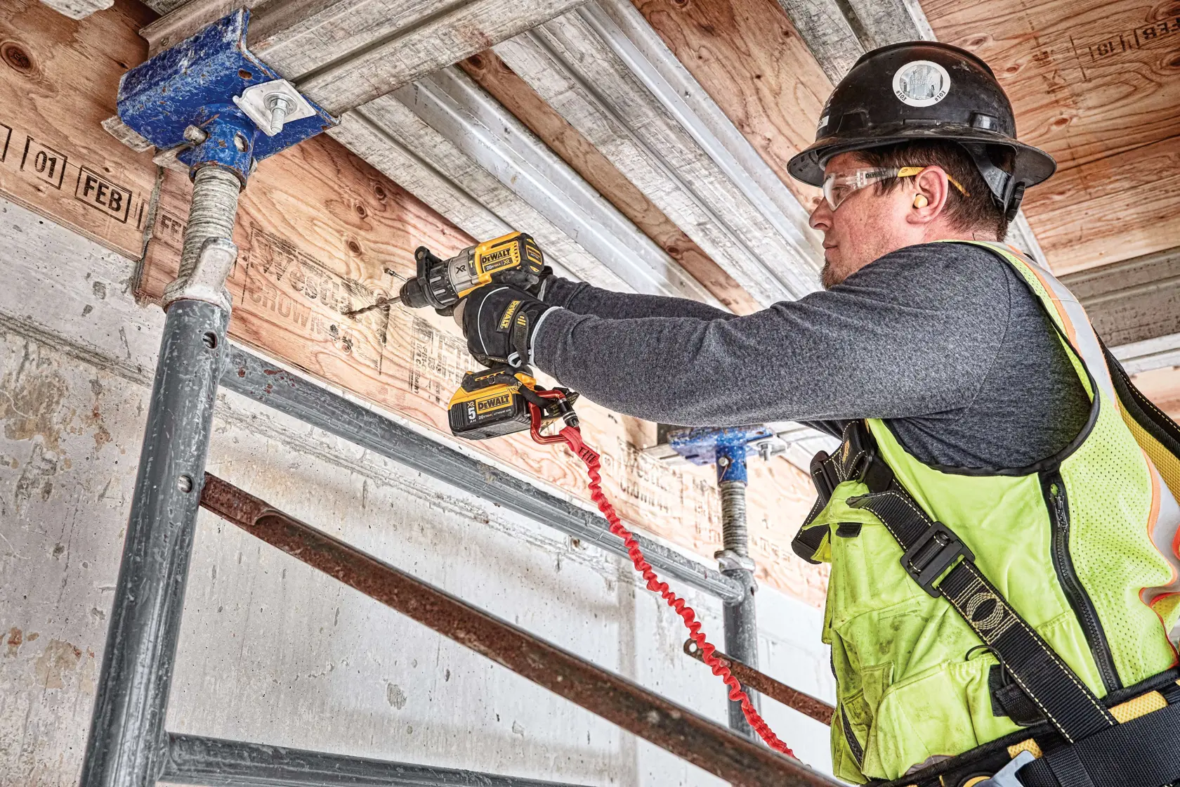 Una persona utilizza un trapano a batteria DEWALT (modello DCD996P2) per forare una trave di legno in un cantiere edile.