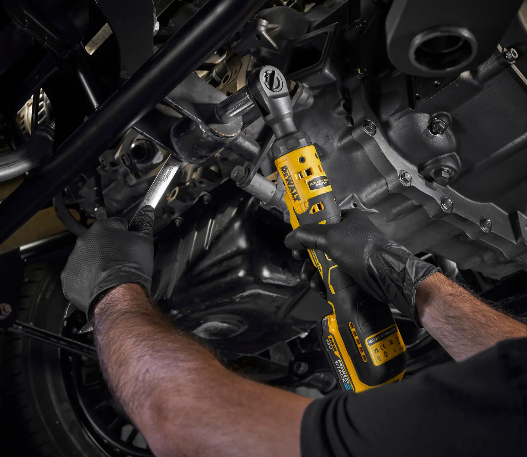 Persona usa un cricchetto DEWALT senza fili su un motore, indossa guanti neri.