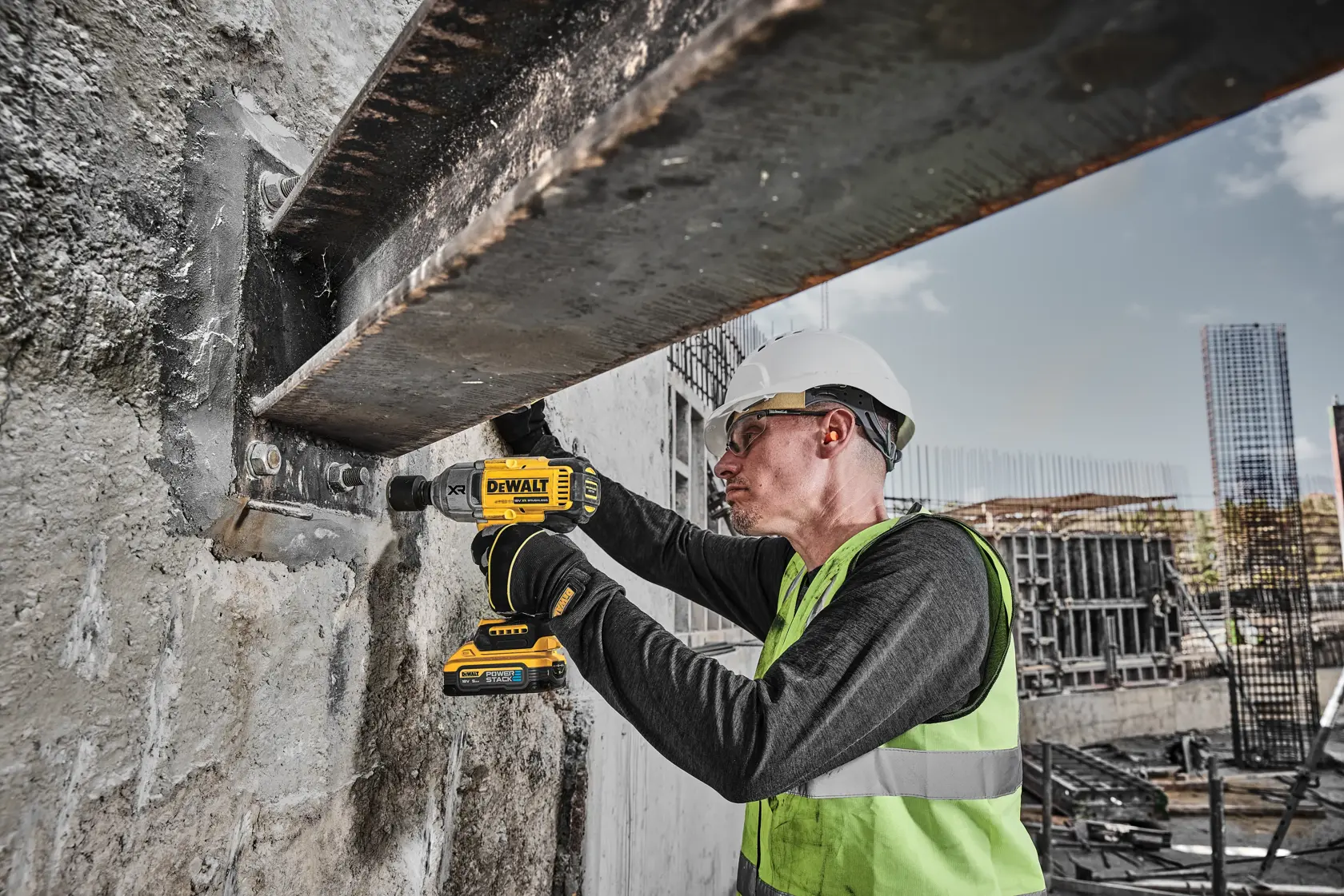 Operaio usa un trapano DEWALT DCF900H2T su una trave in acciaio, con abbigliamento e casco protettivo.