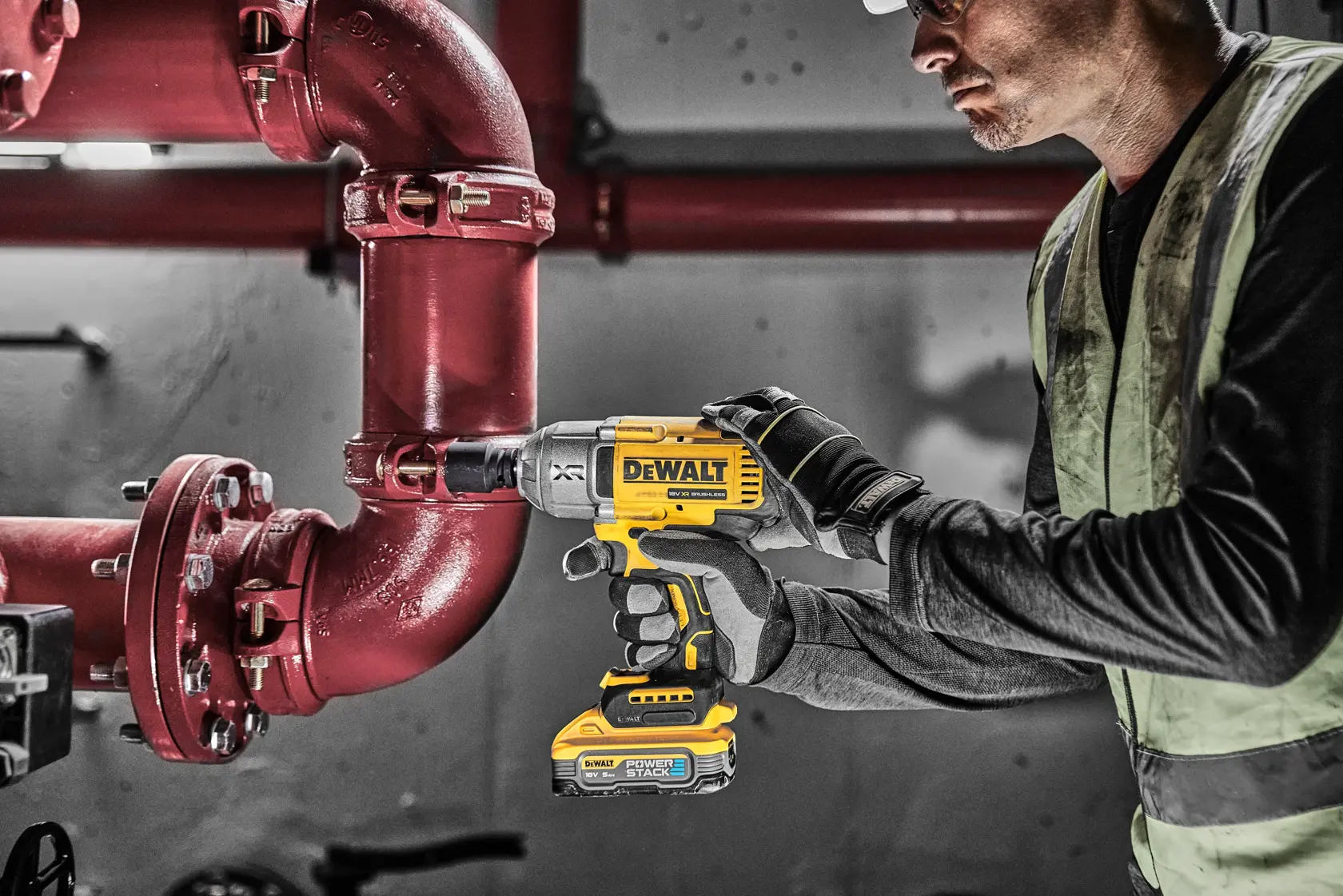 Persona usa avvitatore a impulsi DEWALT DCF900H2T su un tubo rosso in ambiente industriale.