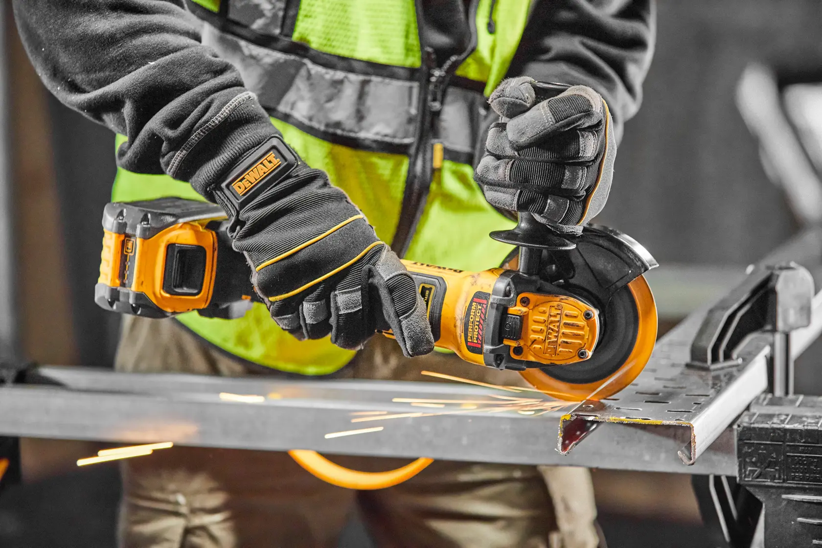 Persona usa una smerigliatrice angolare DEWALT a batteria su metallo, con guanti e gilet di sicurezza.