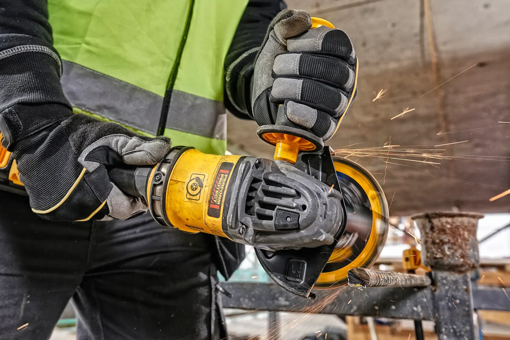 Persona usa smerigliatrice DEWALT DCG418NT su metallo, scintille, con guanti e giubbotto di sicurezza.