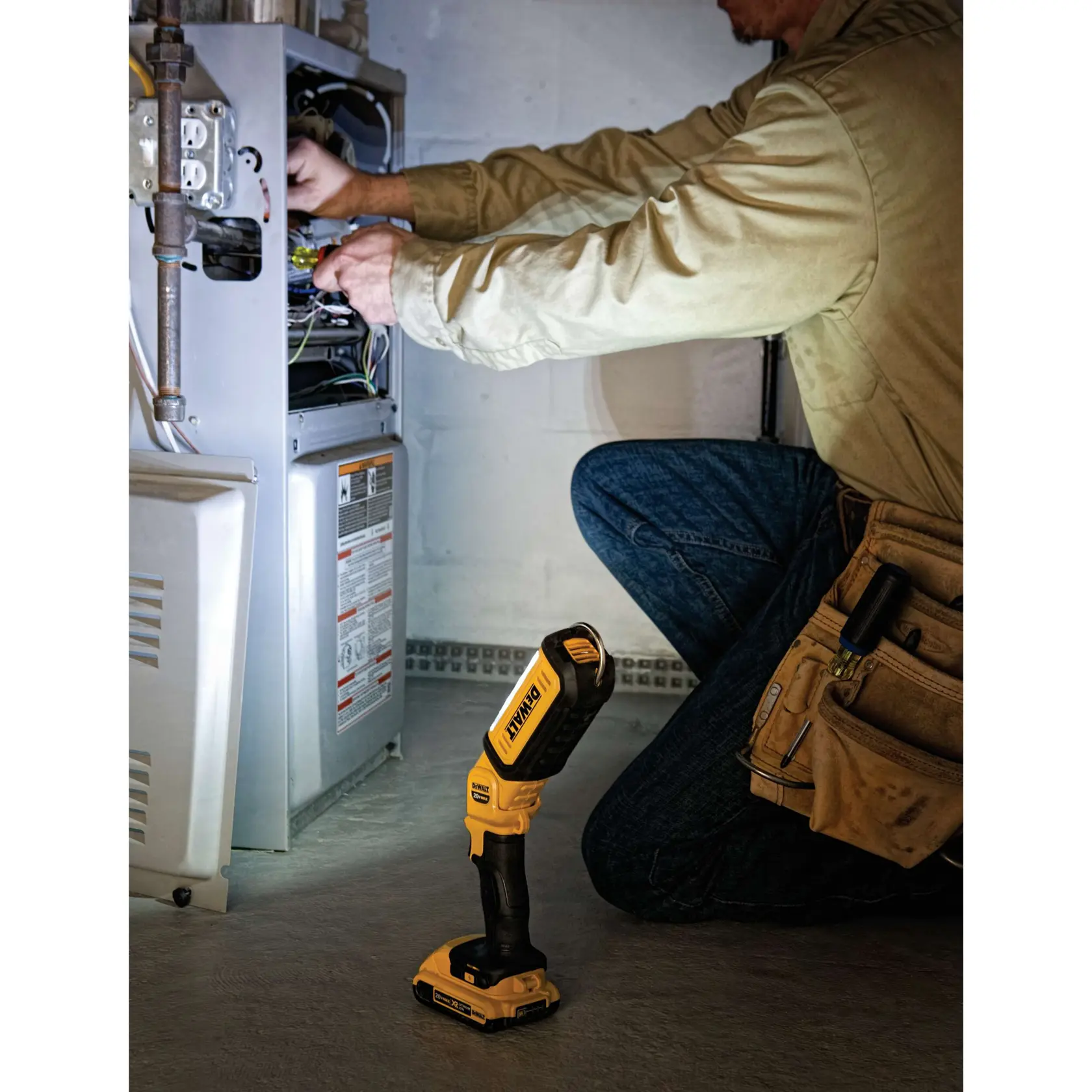 Une lampe de travail LED DEWALT DCL050 est utilisée pour éclairer un système de suspension automobile tandis qu'une personne portant des lunettes de sécurité et des gants travaille avec un autre outil DEWALT.