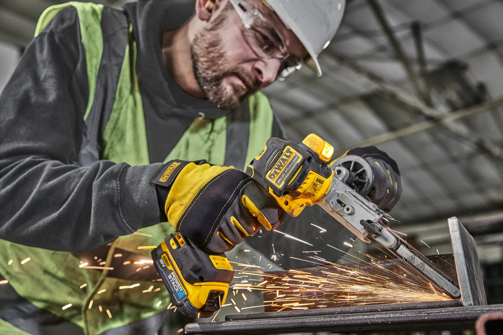Operaio usa levigatrice a nastro DEWALT senza fili su metallo, scintille in ambiente industriale.