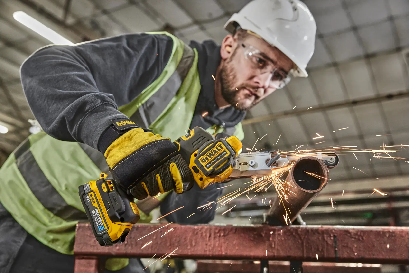 Operaio taglia un tubo metallico con utensile DEWALT senza fili, scintille e protezioni visibili, ambiente industriale.