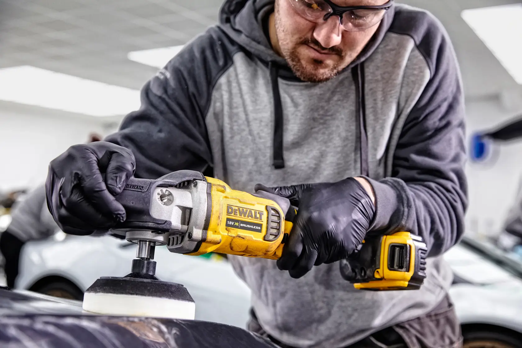 Persona usa lucidatrice DEWALT DCM849P2 su auto in officina, indossa guanti.