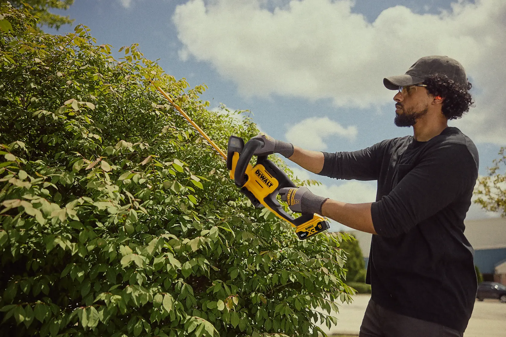 Persona pota cespugli con tagliasiepi DEWALT senza fili all'aperto, giornata di sole.