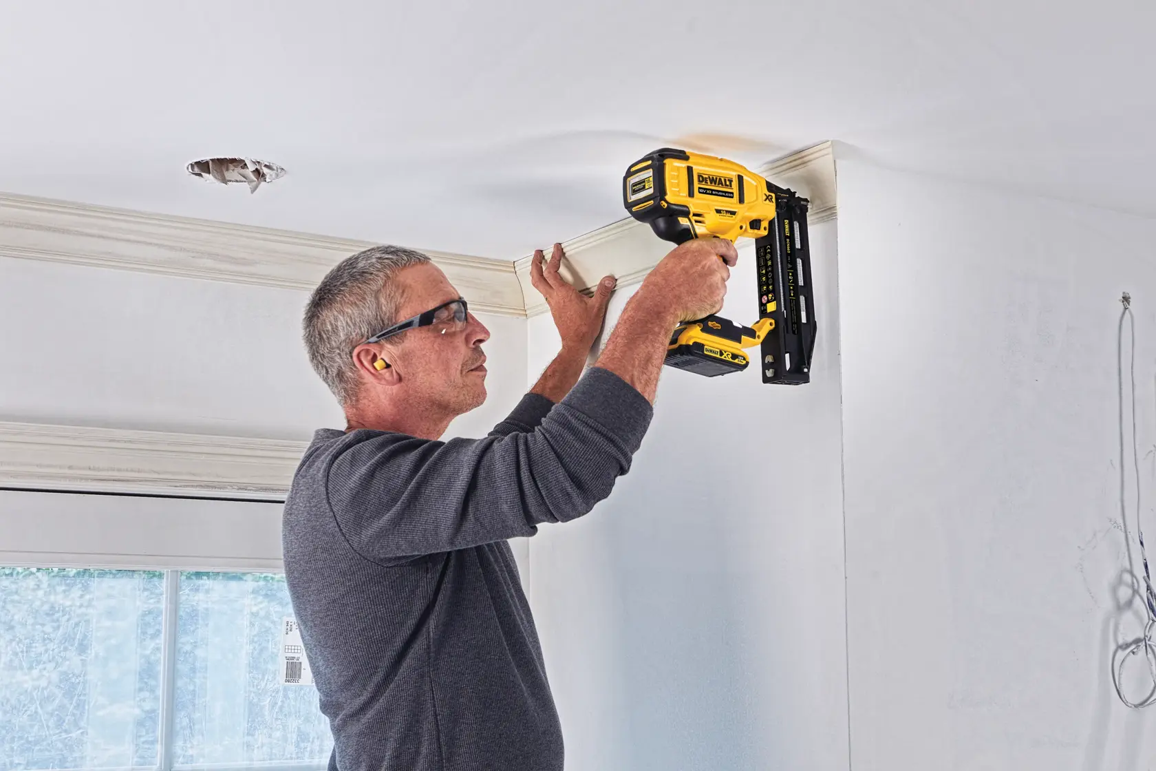Persona usa chiodatrice DEWALT per montare modanatura al soffitto. Modello: DCN662D2.