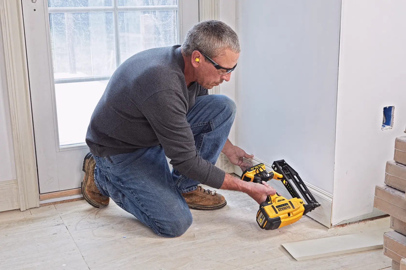 Persona usa un chiodatrice DEWALT senza fili per installare battiscopa vicino a una porta in una stanza rinnovata.