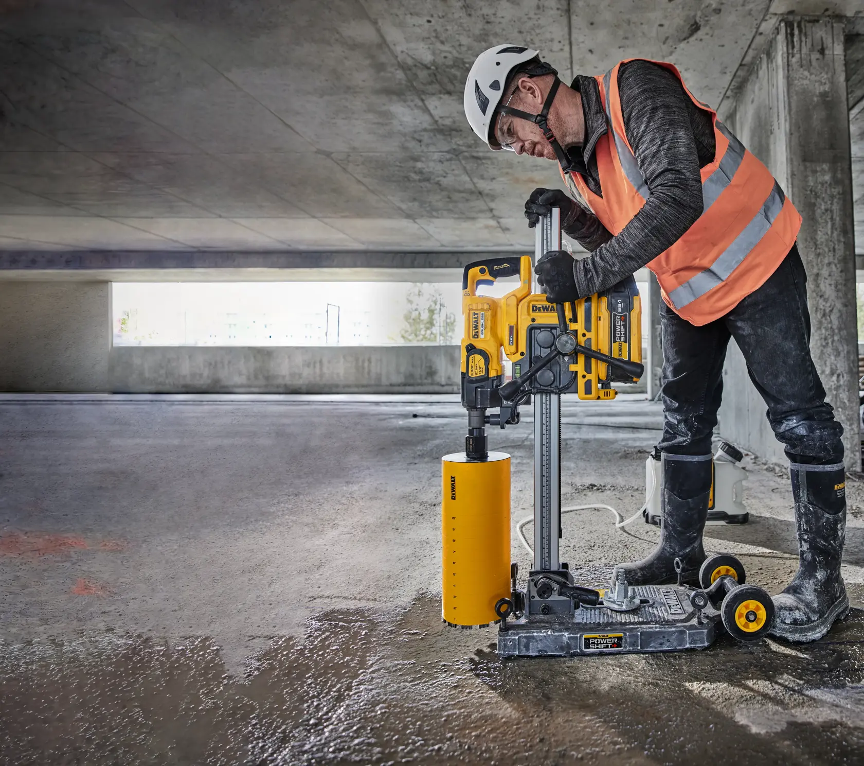 Image showing the DEWALT DCPS151 Powershift core drill stand with a yellow and black drill mounted vertically on a metal rail with wheels. The product includes various accessories such as a feeding lever, vacuum hose connector, clamping nut, screw rod, setting tool, and drop-in pieces. A list of included items is featured in a black and yellow section at the top.