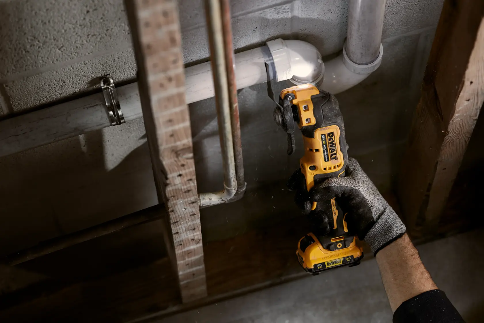 Mano con guanto usa utensile DEWALT senza fili per tagliare tubo vicino a parete e travi in legno.