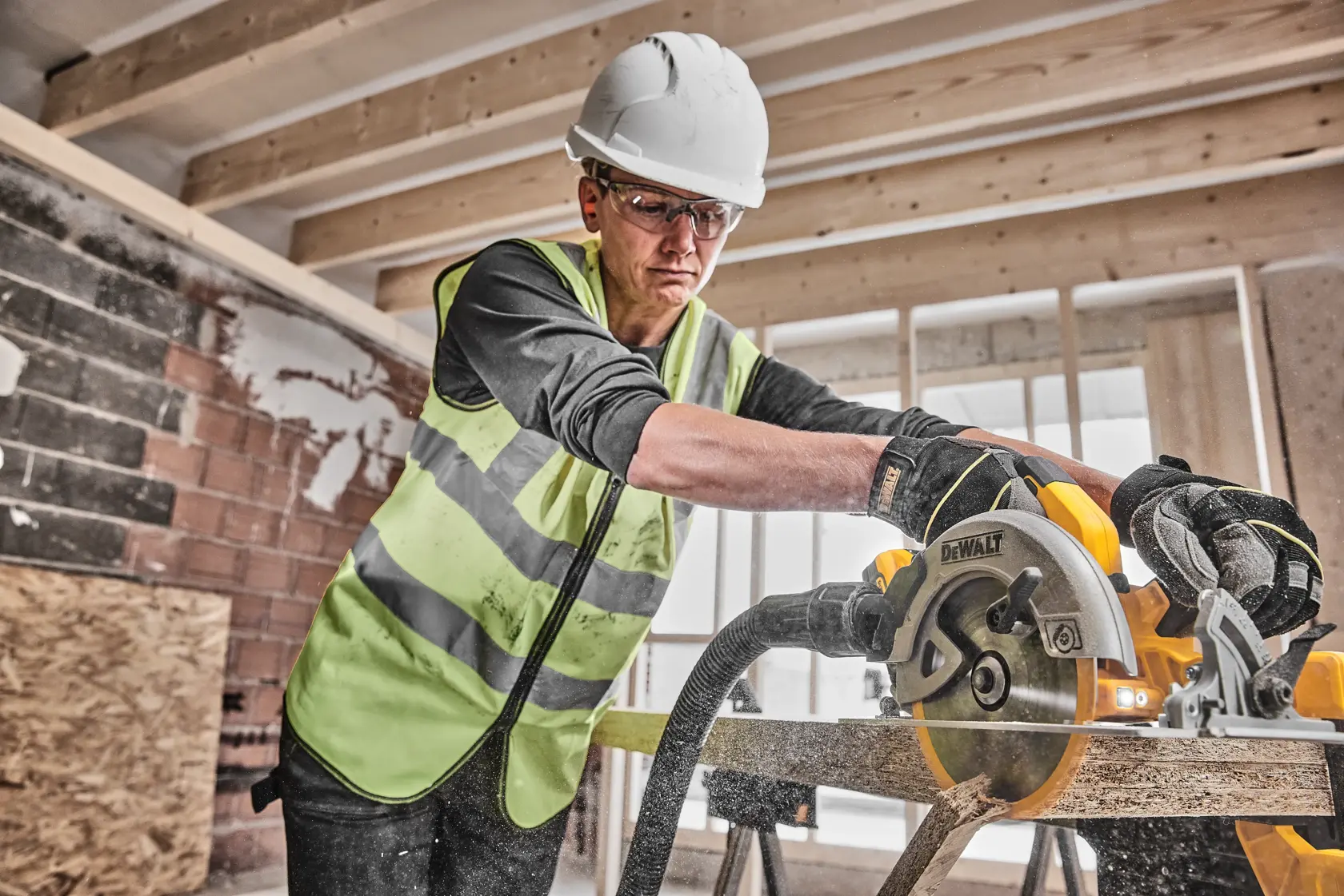 Operaio taglia legno con sega circolare DEWALT in cantiere, indossa gilet e guanti protettivi.