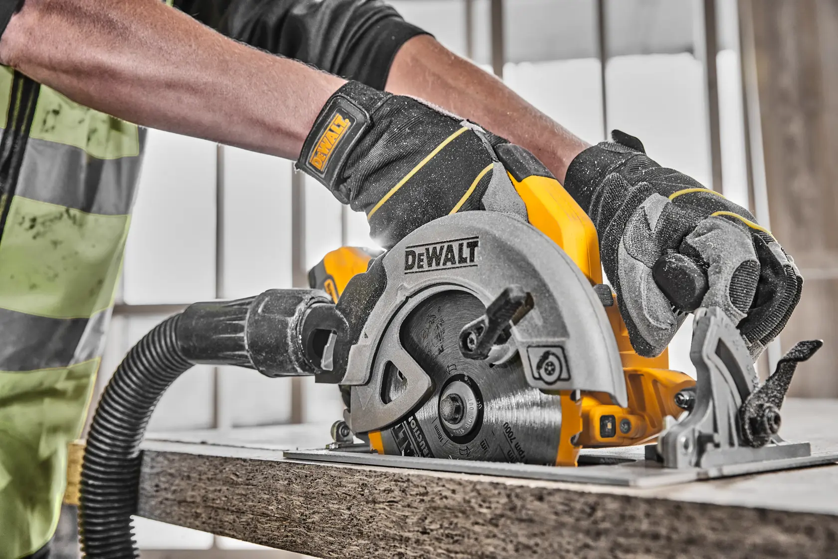 Mani con guanti usano una sega circolare DEWALT senza fili con aspirazione per tagliare il legno.