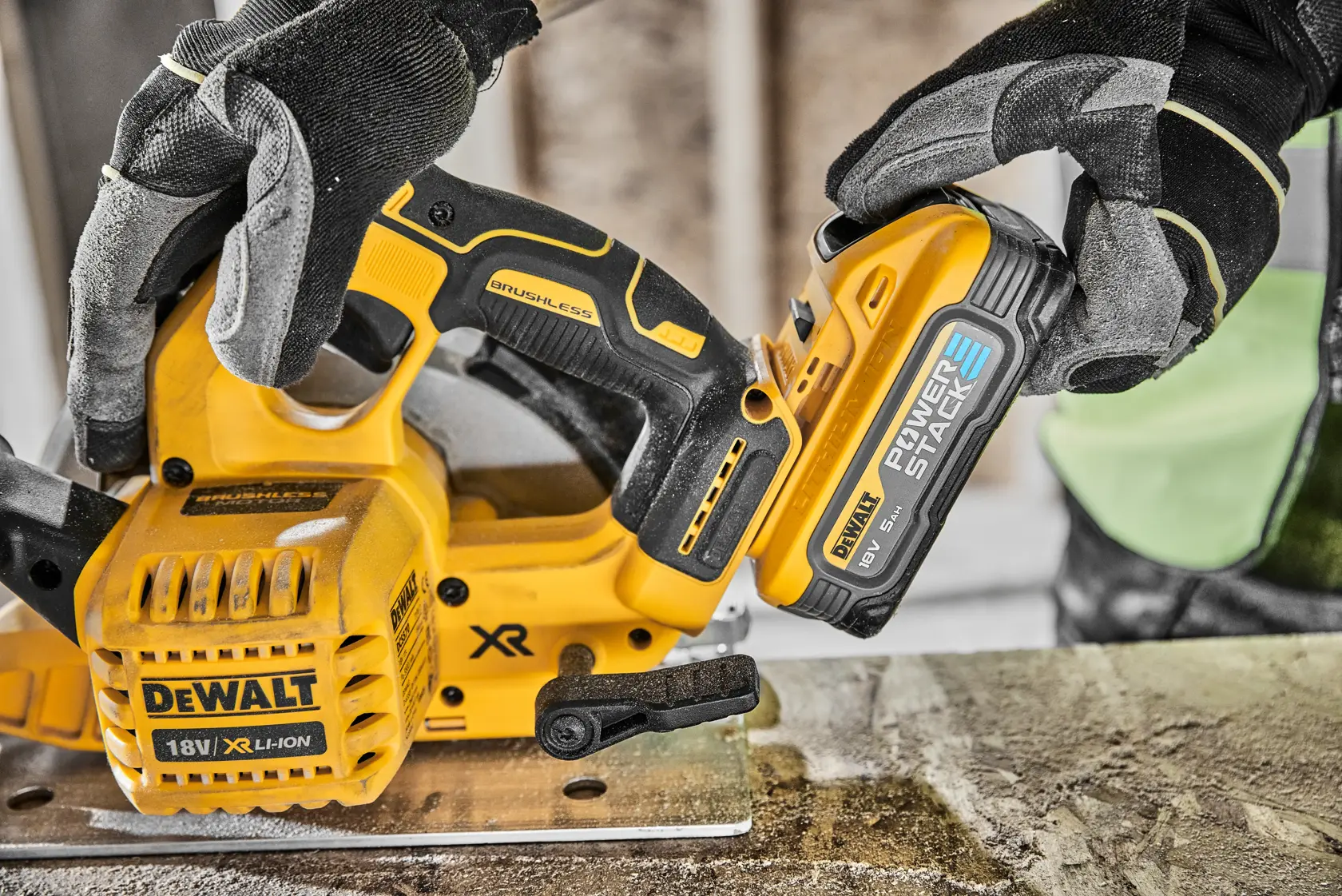 Mani guantate collegano una batteria DEWALT 18V a una sega gialla senza fili su un banco da lavoro.