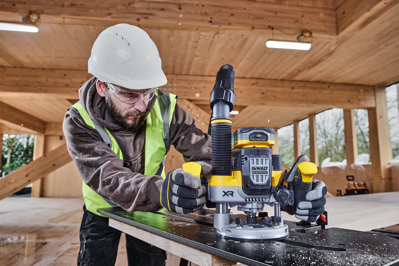 Operaio usa un fresatore DEWALT DCW620H2 su legno, indossando abbigliamento e guanti protettivi.