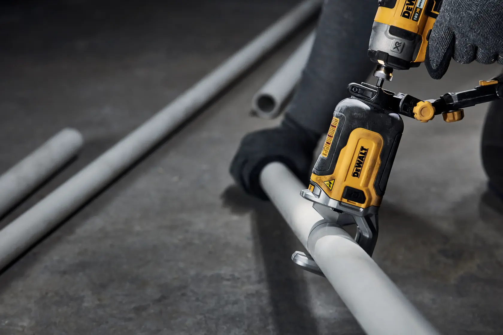 Primo piano di un utensile elettrico DEWALT usato da una persona con i guanti per tagliare un tubo metallico grigio sul pavimento di un laboratorio.