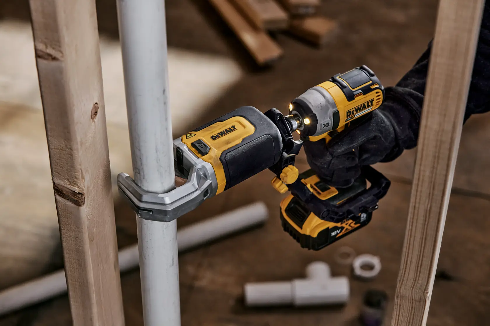 Un utensile elettrico DEWALT DT20560 utilizzato per fissare una staffa a un tubo metallico, tenuto da una persona con guanto. L’utensile è giallo e nero, e sullo sfondo ci sono altri tubi e assi di legno.
