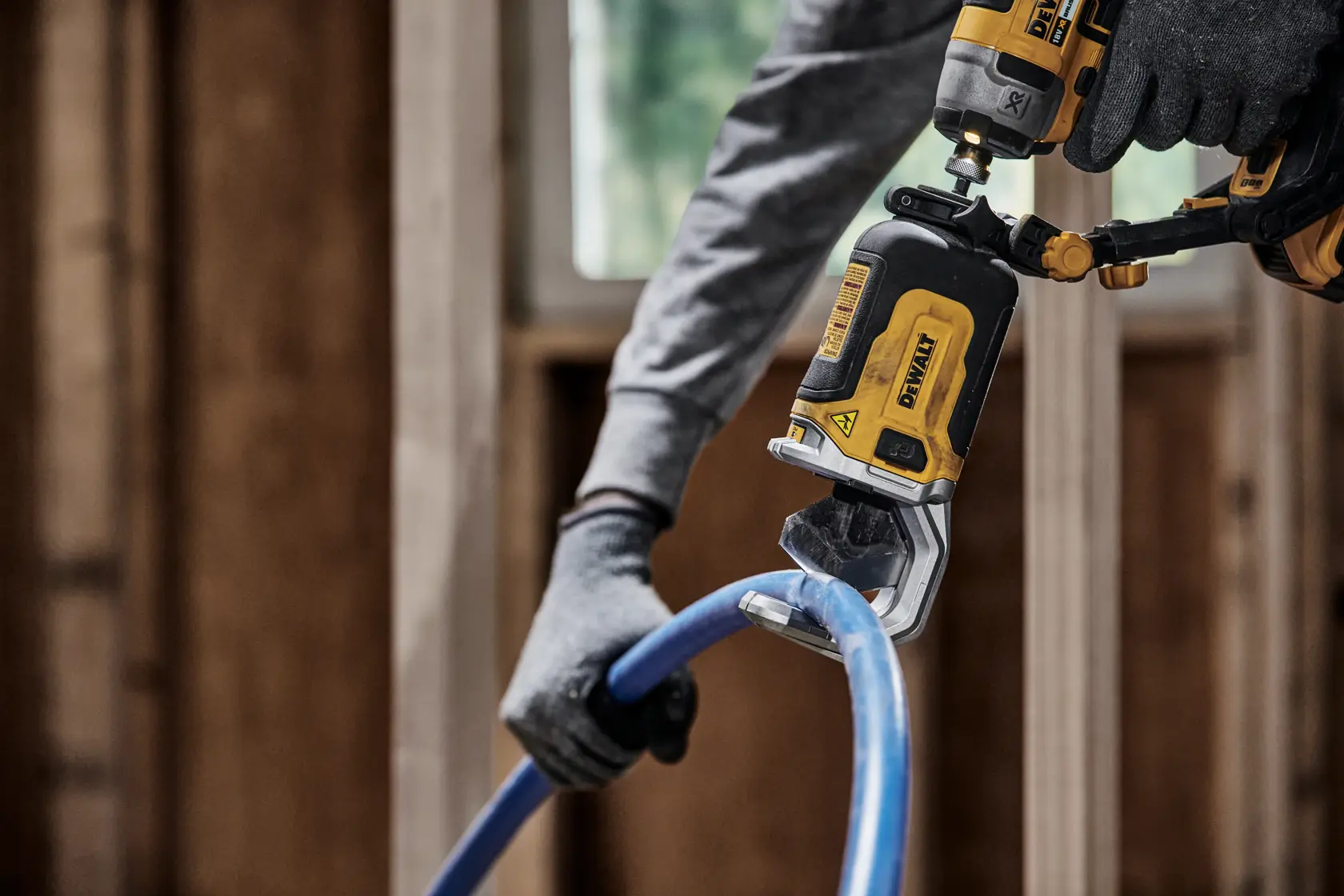 Una persona con guanti utilizza un utensile elettrico DEWALT DT20560 per tagliare un tubo di plastica blu in un contesto di costruzione.