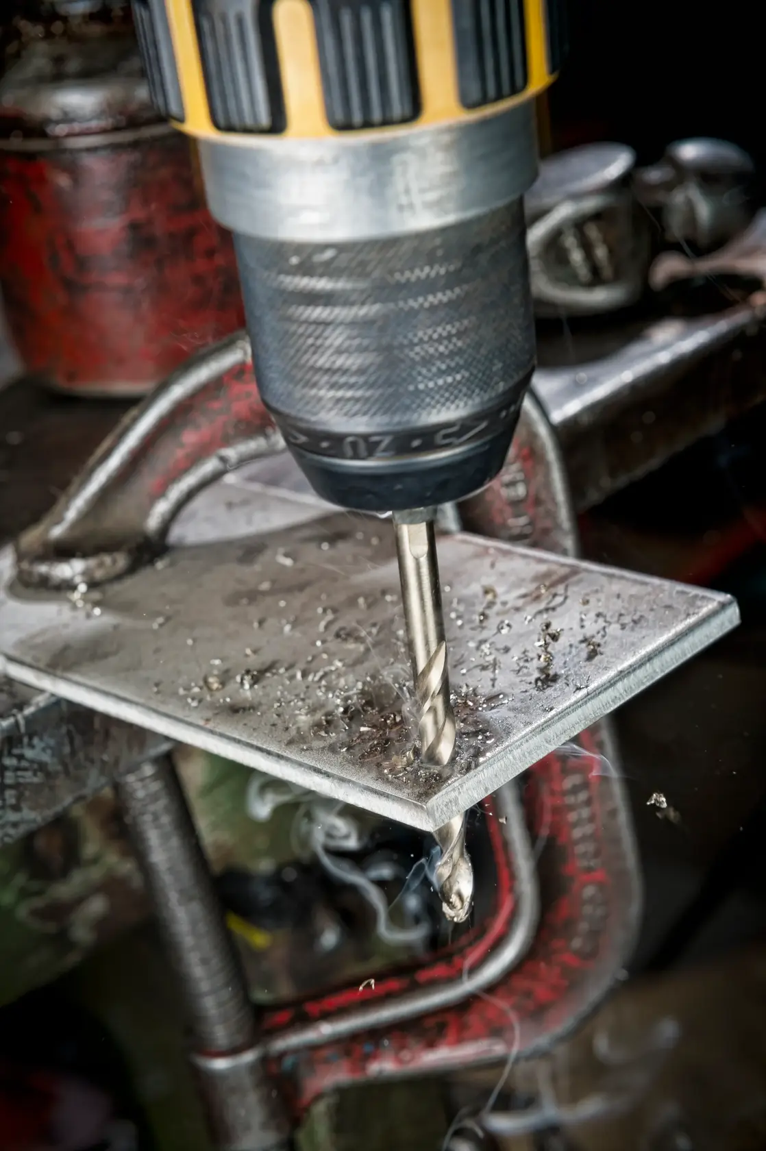 Close-up of a DEWALT drill making a hole in a metal sheet clamped in place, with metal shavings around.
