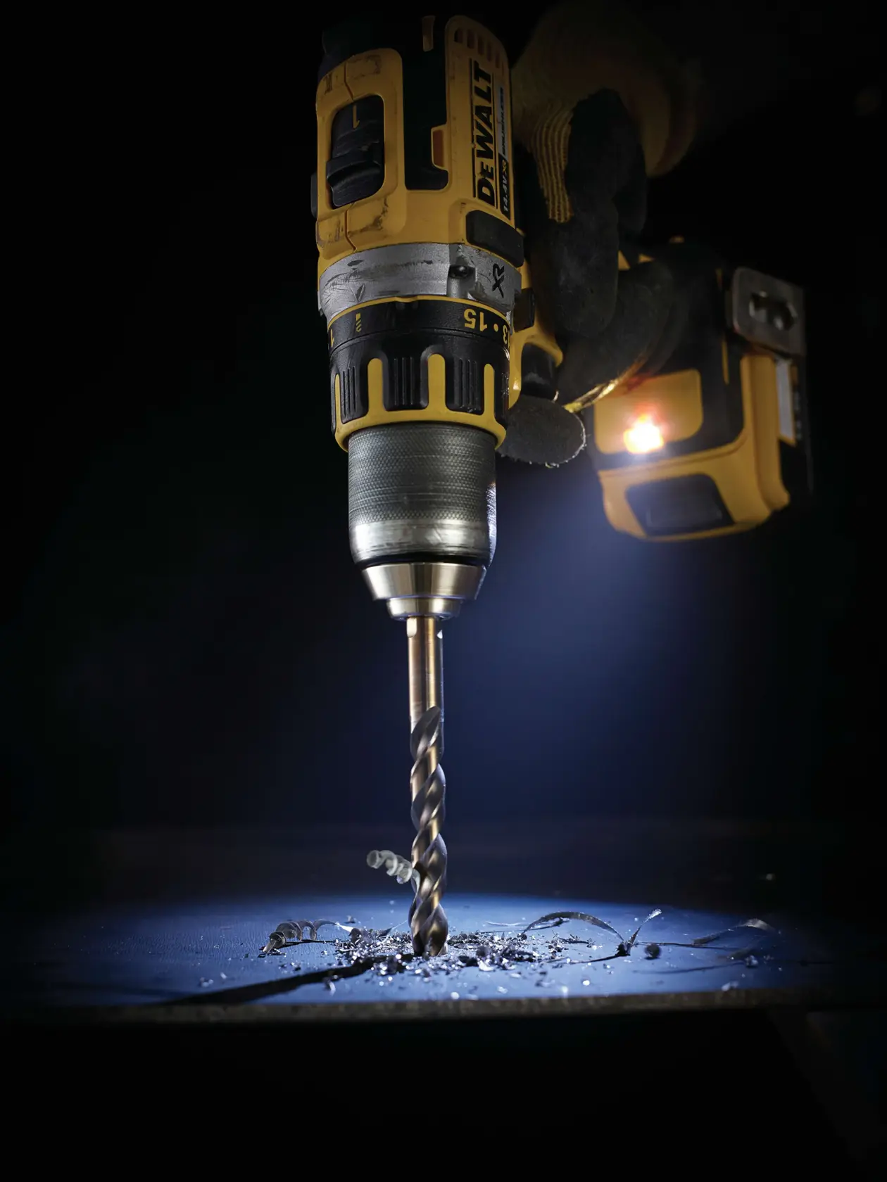 Taladro DEWALT en uso, perforando metal con restos y virutas visibles, resaltado por luz LED.