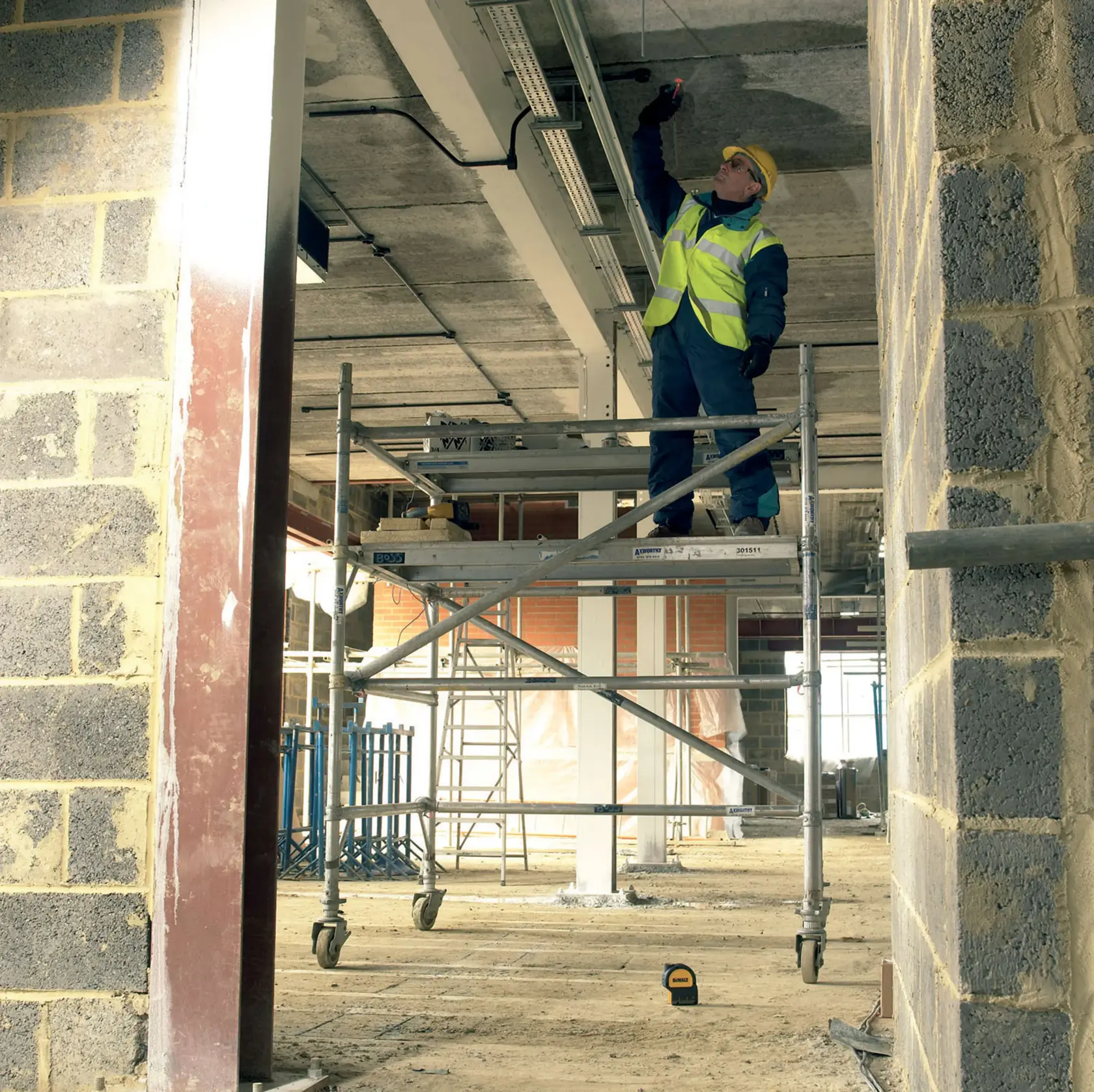 A person is using a DEWALT laser level device to measure and align metal framing on a construction site floor.