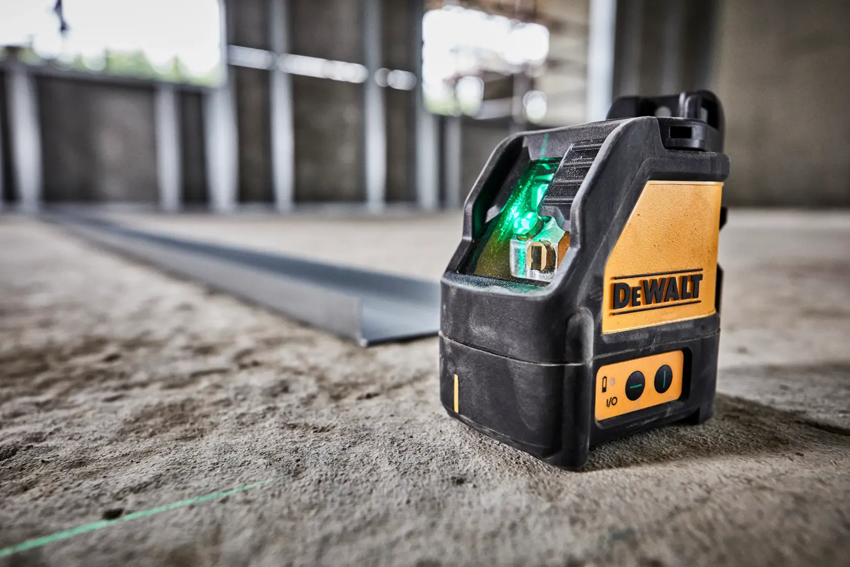 A DEWALT DW088CG green cross line laser level positioned on the floor in a construction site, emitting a visible green laser