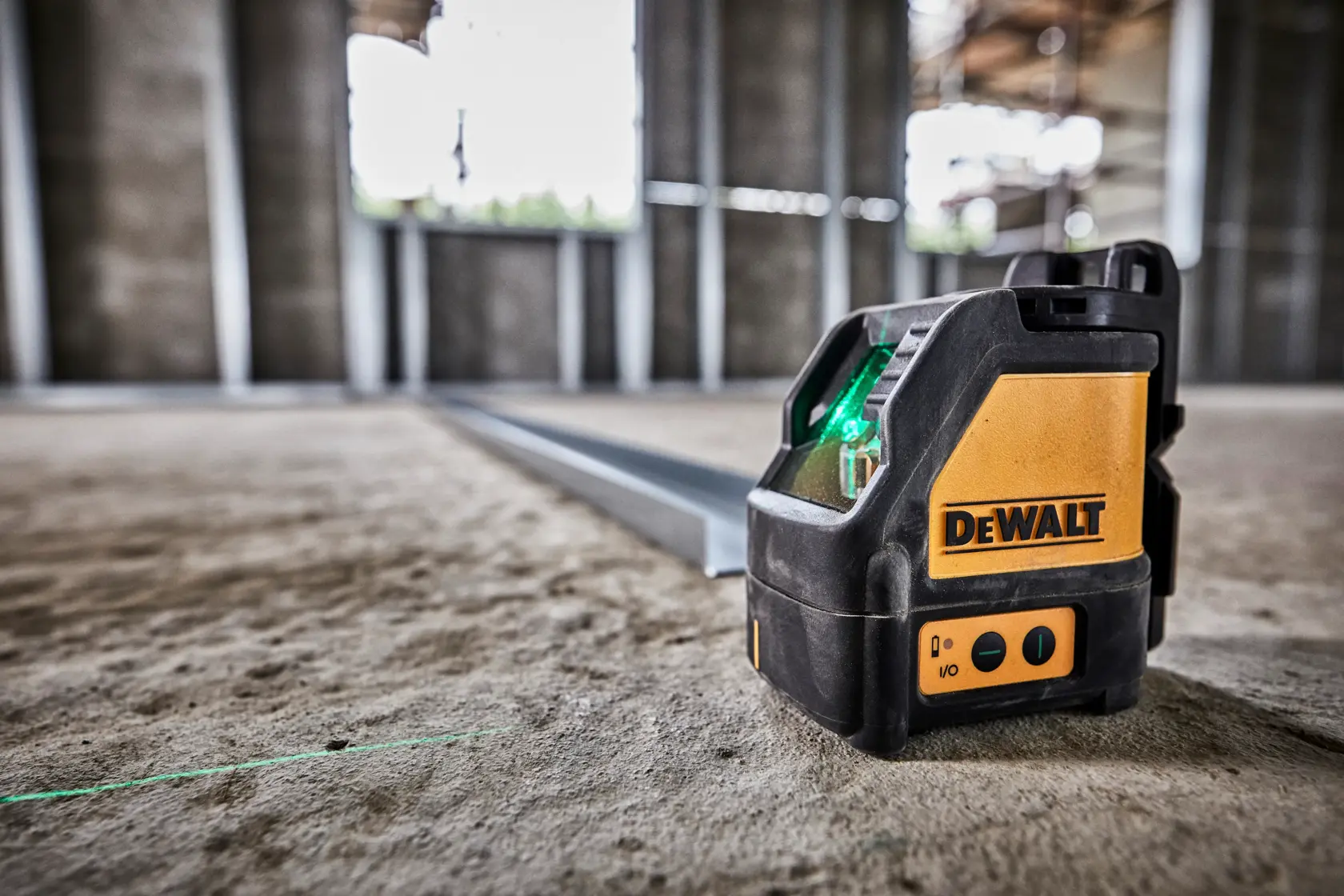 A DEWALT DW088CG green laser level is positioned on a concrete floor in a construction site. The device projects a visible