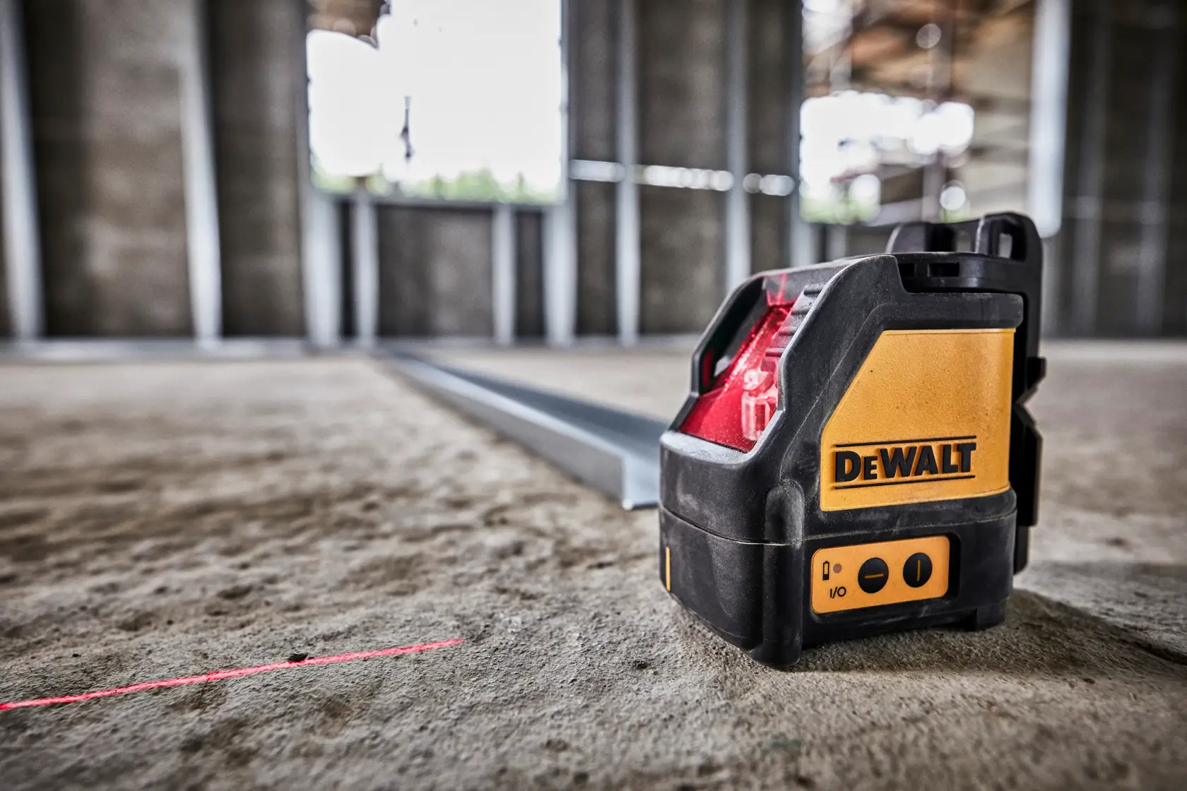 A DEWALT DW088K self-leveling cross line laser level placed on a construction site floor, projecting a visible red laser line used for alignment tasks.