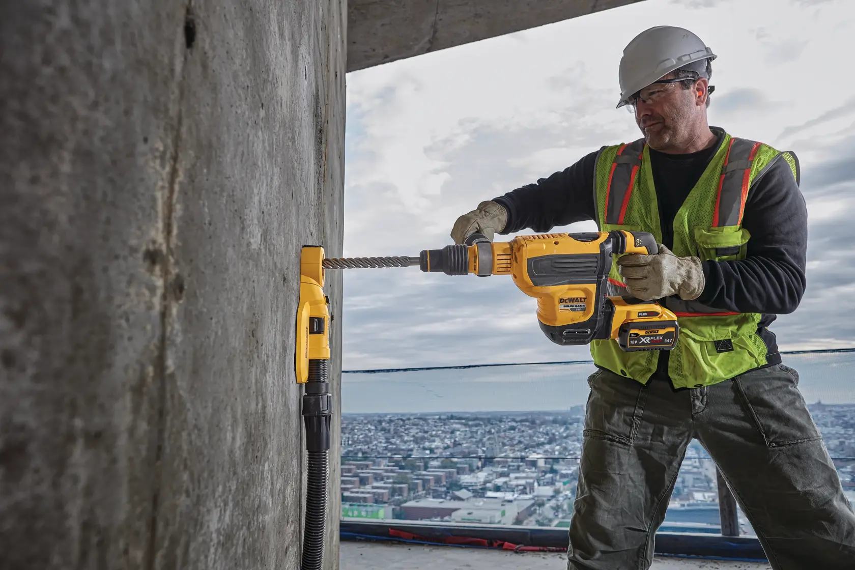 A construction worker using a DEWALT power drill with a dust extraction attachment (SKU: DWH050) to drill into a concrete wall, wearing safety gear including a helmet, gloves, and a high-visibility vest, with a cityscape visible in the background.