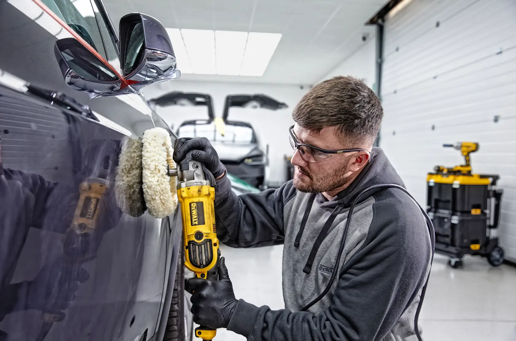 Une personne polit le capot d'une voiture de sport rouge avec une polisseuse DEWALT DWP849X dans un garage.