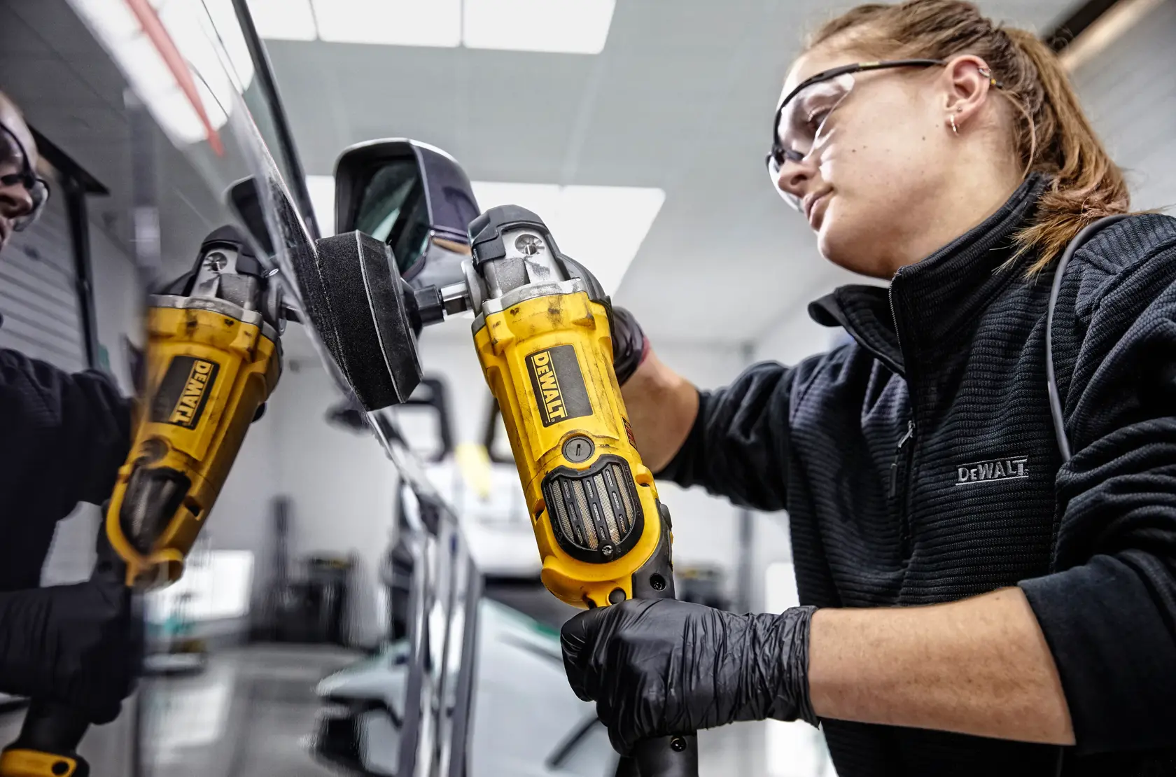Una persona sta lucidando il cofano di un'auto sportiva rossa con una lucidatrice DEWALT DWP849X in un garage.