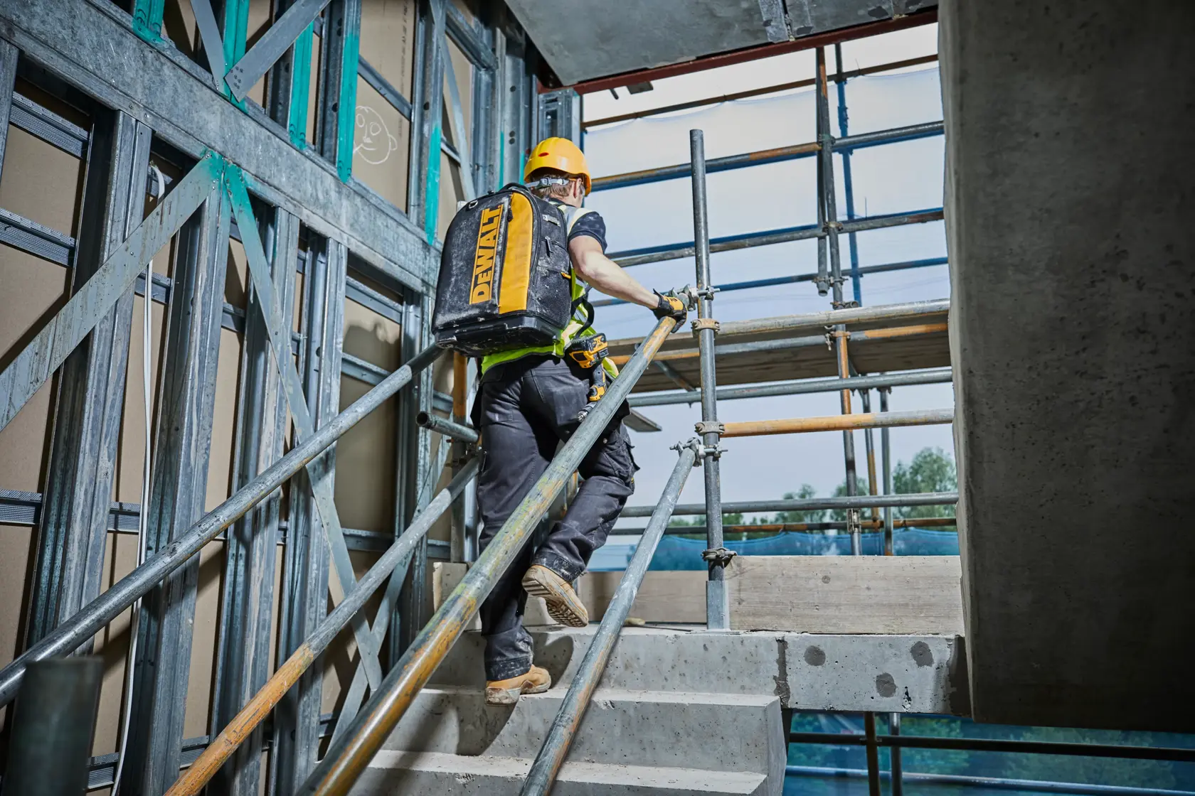 Operaio sale le scale in cantiere con uno zaino giallo DEWALT.