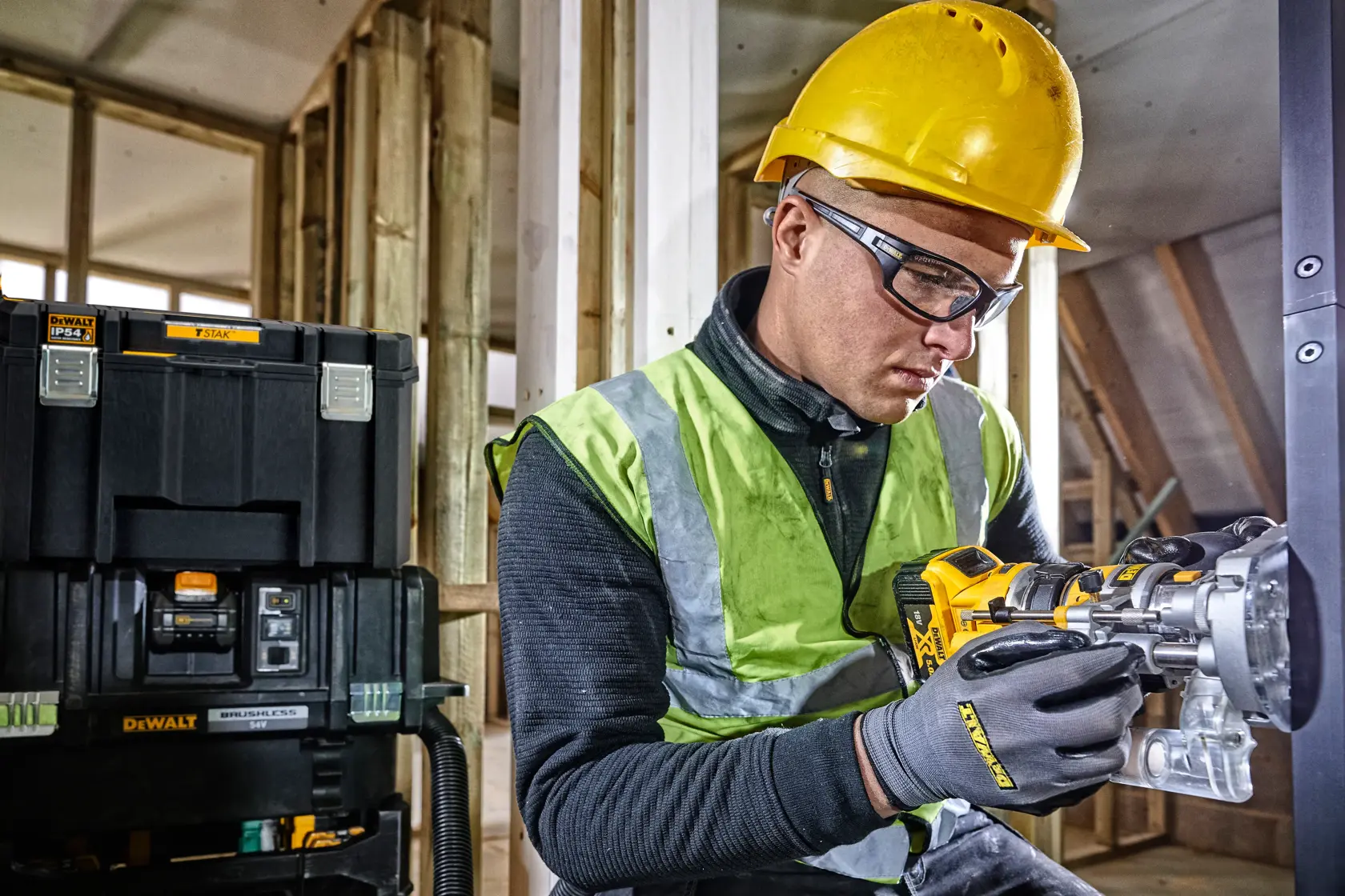 Operaio con casco usa utensile DEWALT, scatola DEWALT sullo sfondo in cantiere.